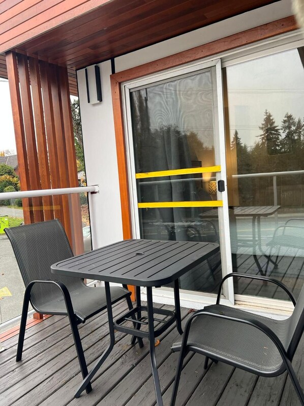 Een terras met een tafel, twee stoelen, een glazen schuifdeur en een houten leuning.