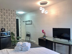 Habitación de hotel con cama, televisor, microondas, toallero y una planta pequeña.