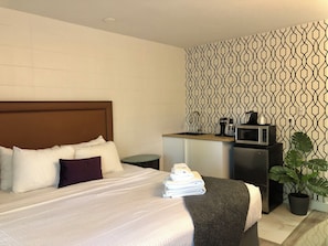 Una habitación de hotel con una cama, una pequeña kitchenette, una planta en maceta y una pared con diseño.