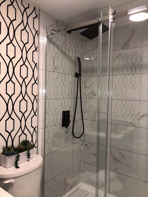 Un box de ducha moderno con puerta de vidrio, un cabezal de ducha manual y un panel de control en la pared.