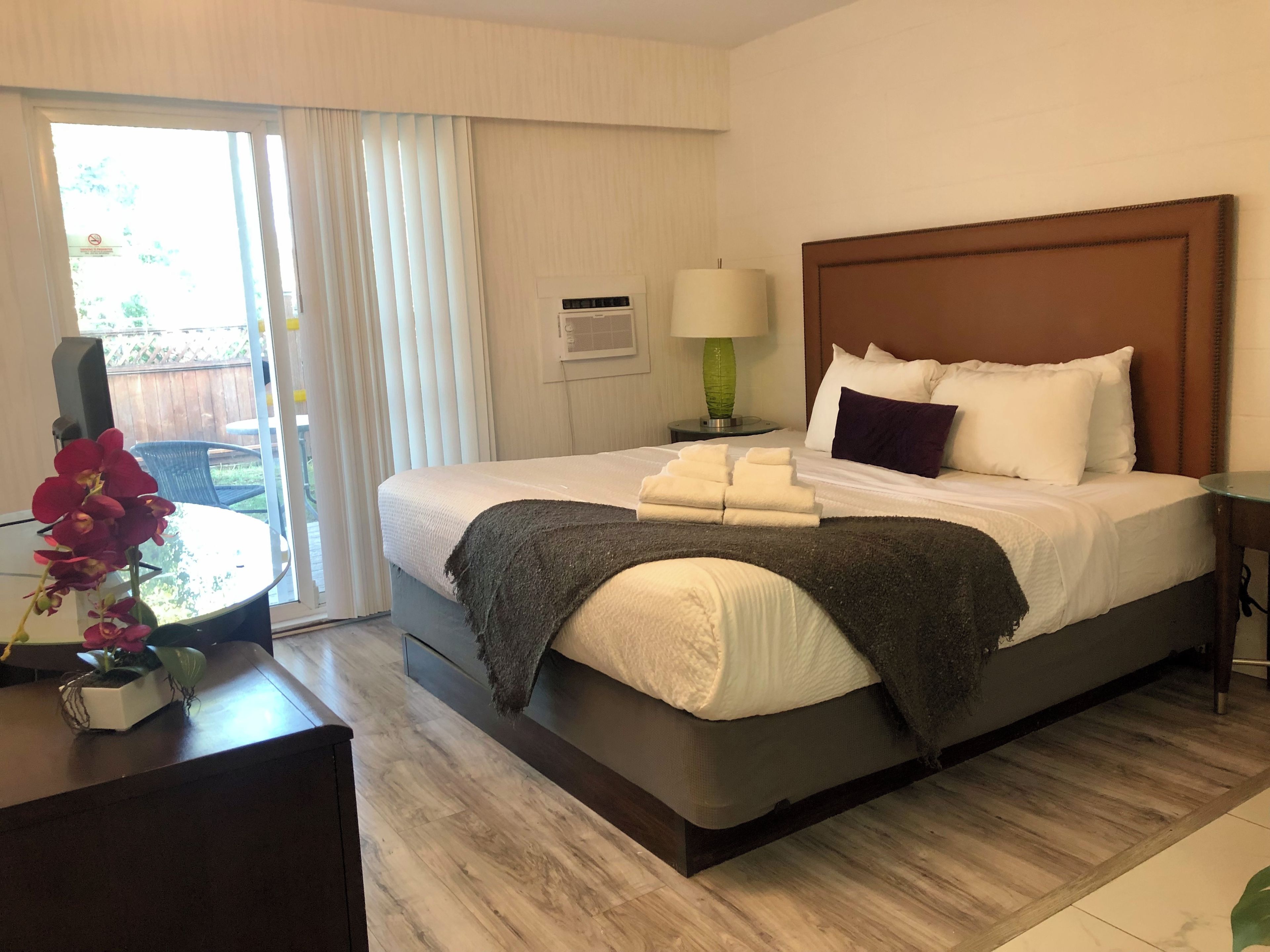 Habitación de hotel con cama, mesita de noche, lámpara y vistas al exterior.