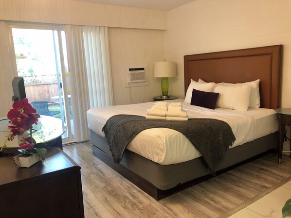 Habitación de hotel con cama, mesita de noche, lámpara y vistas al exterior.