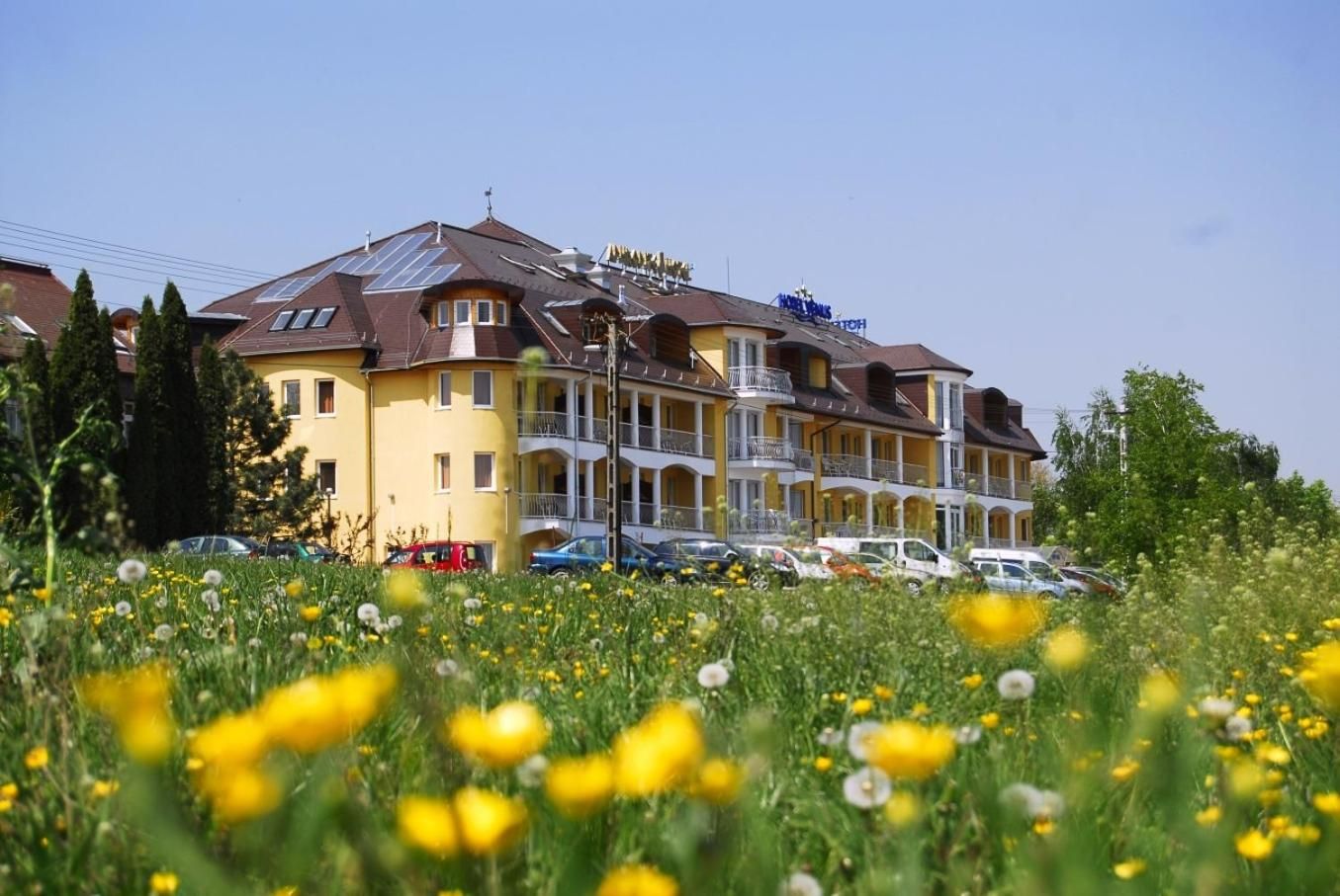 Ein mehrstöckiges Hotel mit Balkonen, einem Parkplatz und einem Feld mit gelben Blumen im Vordergrund.