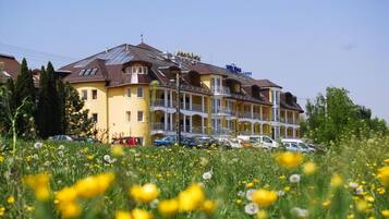 Ein mehrstöckiges Hotel mit Balkonen, einem Parkplatz und einem Feld mit gelben Blumen im Vordergrund.