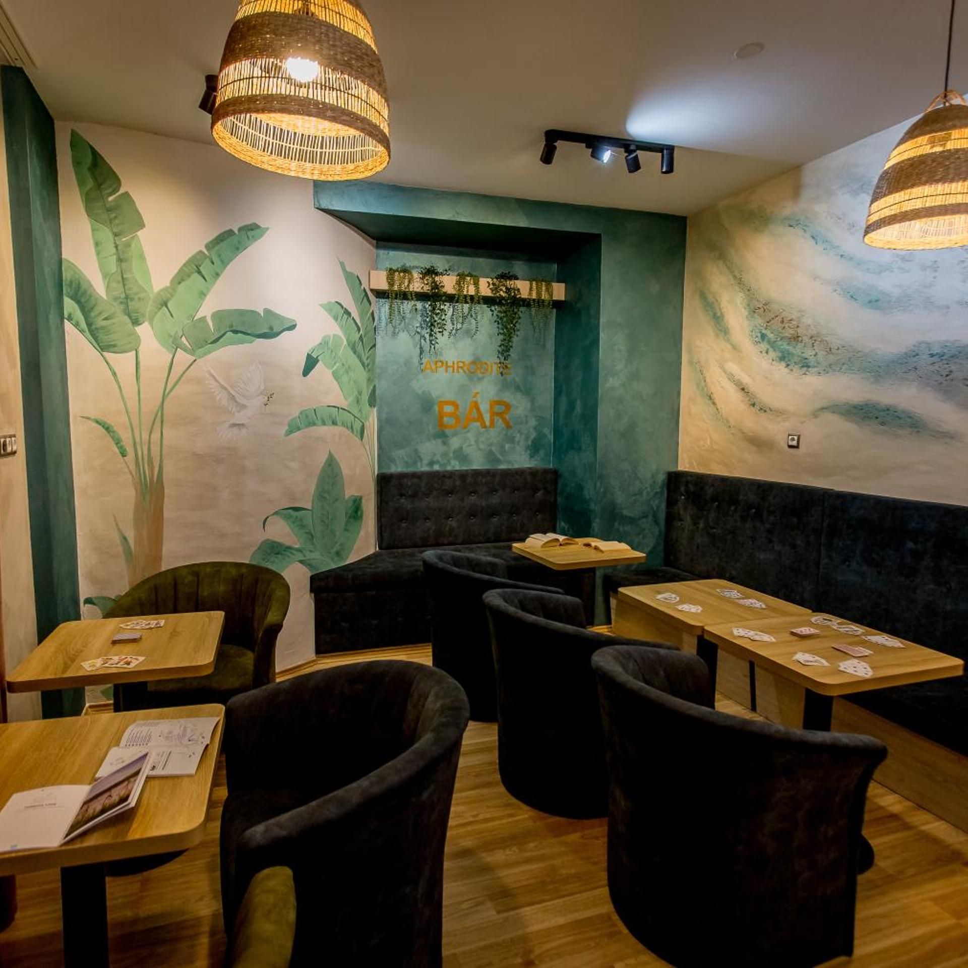 Eine gemütliche Bar mit Holztischen, gepolsterten Sitzgelegenheiten und einer Wandmalerei von tropischen Blättern.