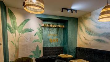 Eine gemütliche Bar mit Holztischen, gepolsterten Sitzgelegenheiten und einer Wandmalerei von tropischen Blättern.