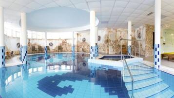 Ein Hallenbad mit Fliesenboden, umgeben von Liegestühlen und einer Sitzgelegenheit mit Tischen.