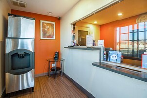 A compact hotel room with a kitchenette, a water dispenser, a small table, and a window with a view.