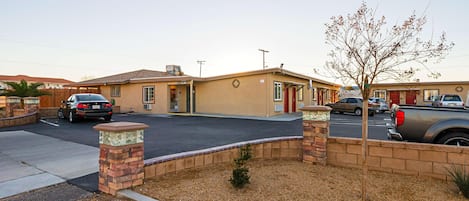 A residential area with a single-story house, a driveway, and parked cars.