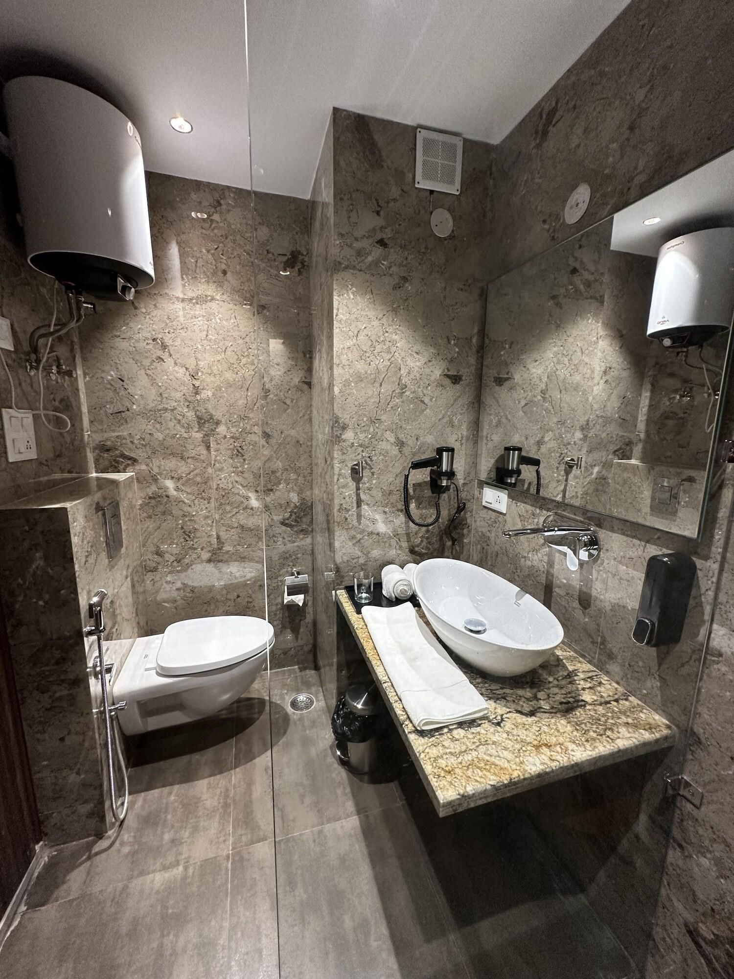 A modern bathroom with a marble wall, a white sink, a toilet, a handheld showerhead, and a mirror.