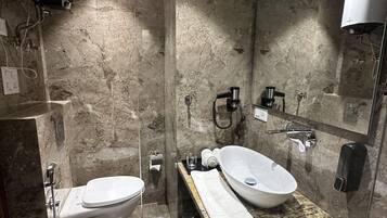 A modern bathroom with a marble wall, a white sink, a toilet, a handheld showerhead, and a mirror.