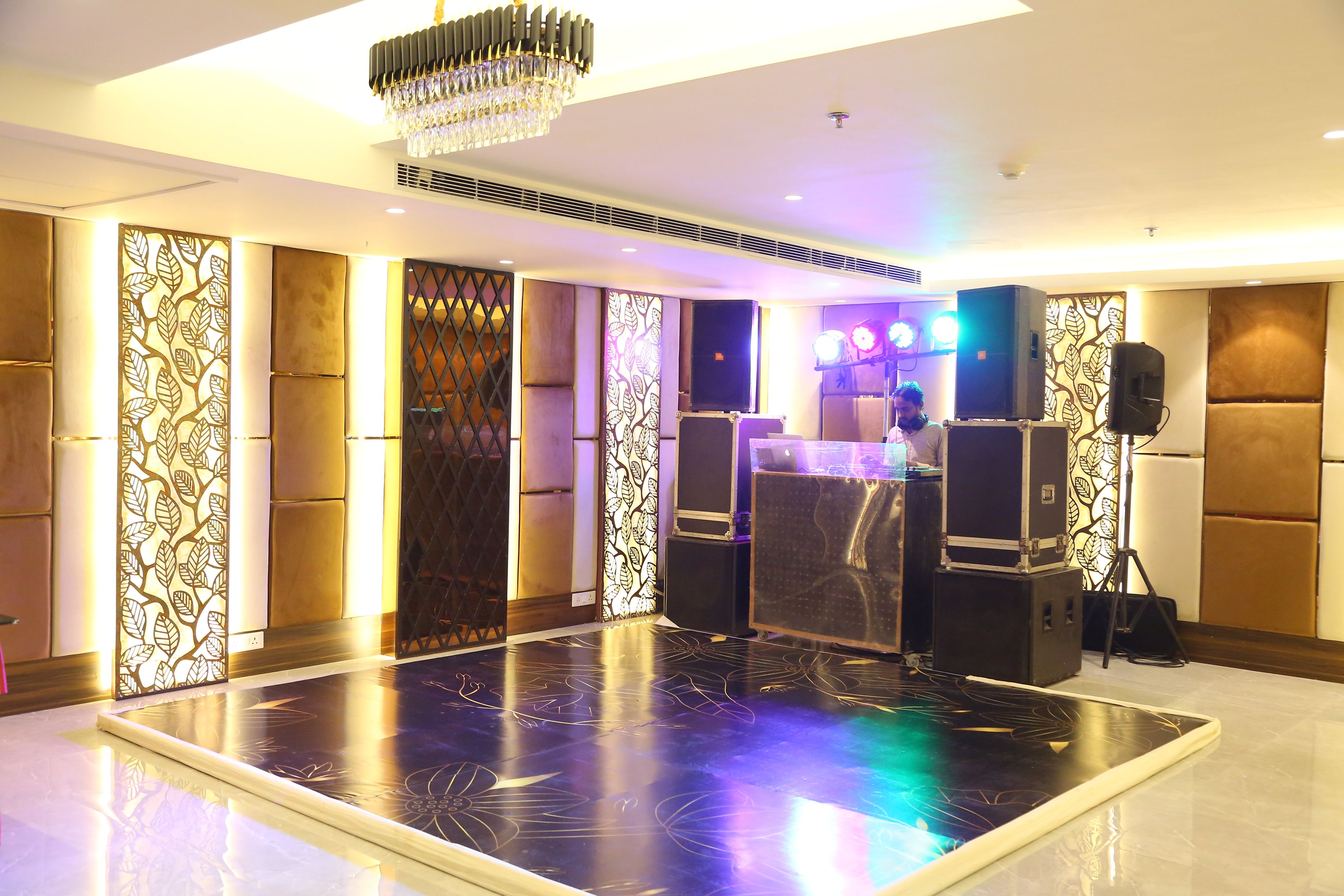 A spacious room with a large black floor, a chandelier, and a bar area with speakers.