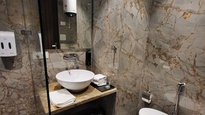 Moderni kylpyhuone, jossa on marmoripintainen seinäallas, suuri pesuallas, wc ja lasiseinällä erotettu suihkutila.