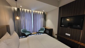 Hotellihuone, jossa on suuri sänky, kaksi nojatuolia, pieni pöytä, televisio ja verhot.