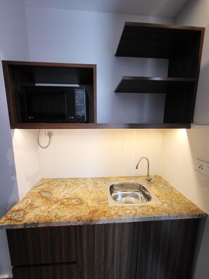 Una cocina con encimera de granito, pileta de acero inoxidable y un microondas sobre una repisa de madera.