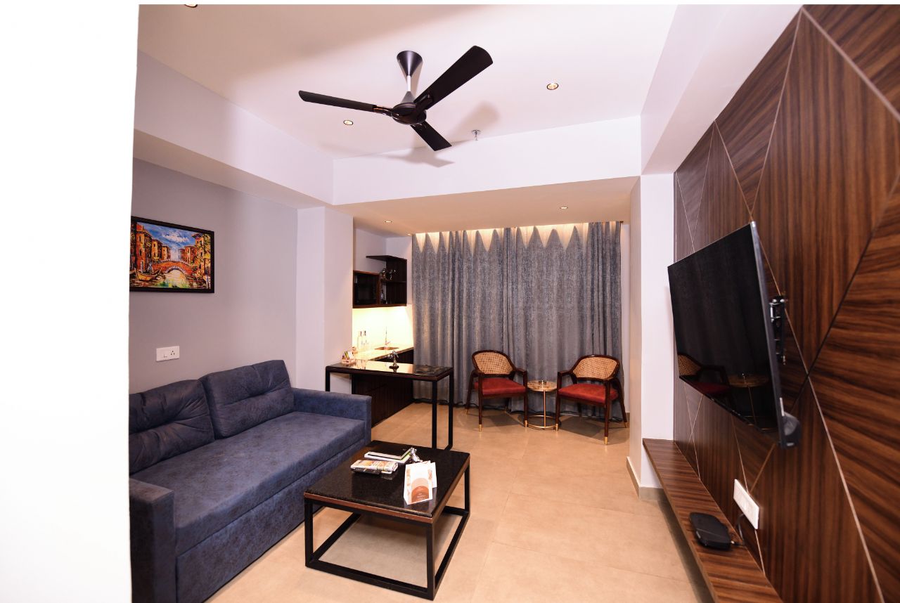 A modern living room with a sofa, coffee table, and chairs, a ceiling fan, and a TV mounted on a wooden wall.