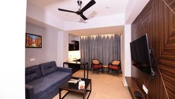 A modern living room with a sofa, coffee table, and chairs, a ceiling fan, and a TV mounted on a wooden wall.