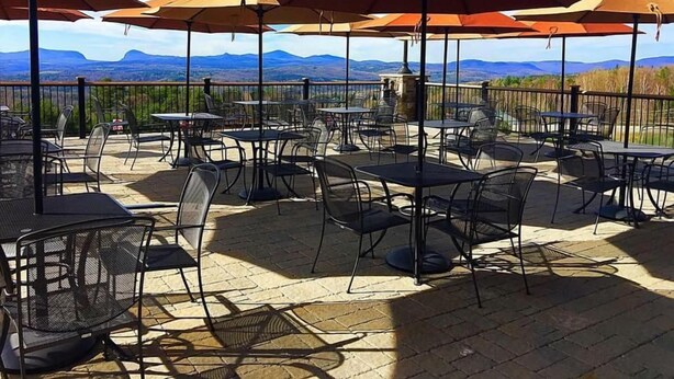 Une terrasse extérieure avec des tables et des chaises, entourée de parasols orange, offrant une vue sur un paysage montagneux.