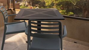 Varanda com duas cadeiras e uma mesa, com vista para um horizonte urbano com edifícios altos e uma árvore.