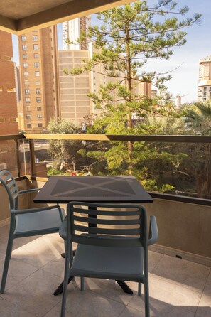 A balcony with two chairs and a table, overlooking a cityscape with tall buildings and a tree. - Torre San Diego (Benidorm)