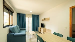 Un espacio habitable compacto con sofá, una mesa de comedor y un televisor sobre una estantería de madera.