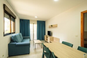 A compact living space with a sofa, a dining table, and a TV on a wooden shelf. - Torre San Diego (Benidorm)