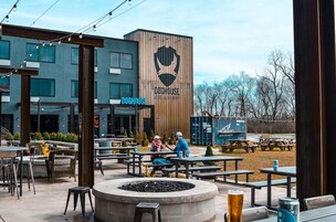 An outdoor seating area with tables and chairs, a wooden building with a sign reading 'DOGHOUSE HOTEL & BREWERY', and a clear sky.