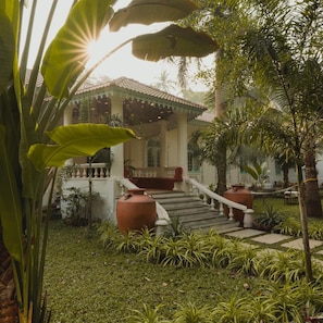 A traditional building with a tiled roof, a staircase leading to a porch, and a well-maintained garden with various plants. - Brij Casa Susegad, Goa (Loutolim)
