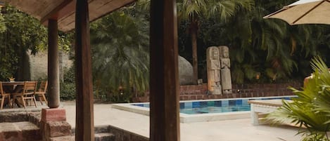A covered outdoor area with a pool, stone steps, and tropical vegetation.
