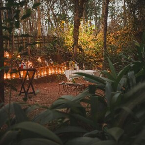 An outdoor dining area with tables and chairs, surrounded by trees and illuminated by string lights. - Brij Casa Susegad, Goa (Loutolim)