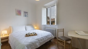 A bedroom with a bed, bedside lamps, a chair, a table, and a window with a view.