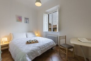 Un dormitorio con cama, lámparas de noche, una silla, una mesa y una ventana con vistas.