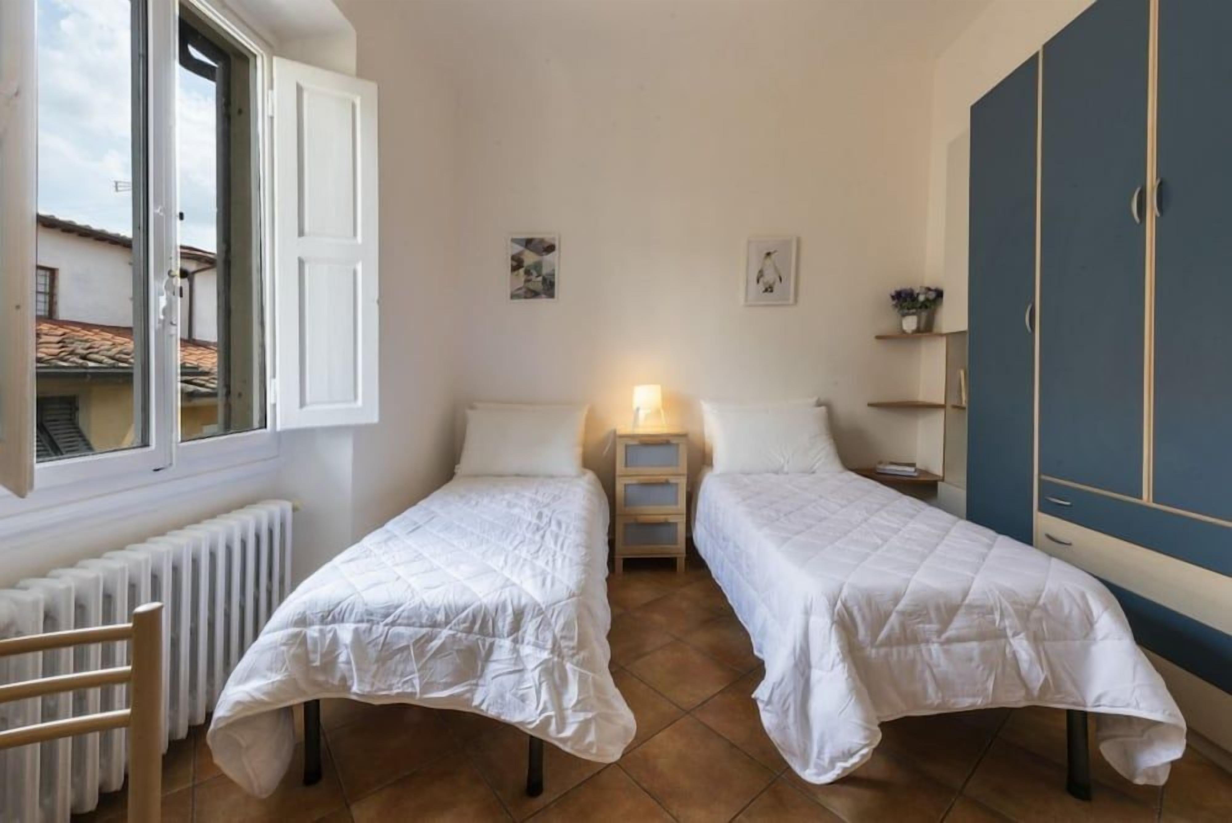 A room with two beds, a radiator, a window, a nightstand, and a wardrobe.