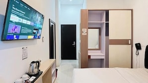 A hotel room with a bed, a TV mounted on the wall, a bedside table with a kettle, and a wardrobe. - Amaze Hotel Kediri (Ngasem)