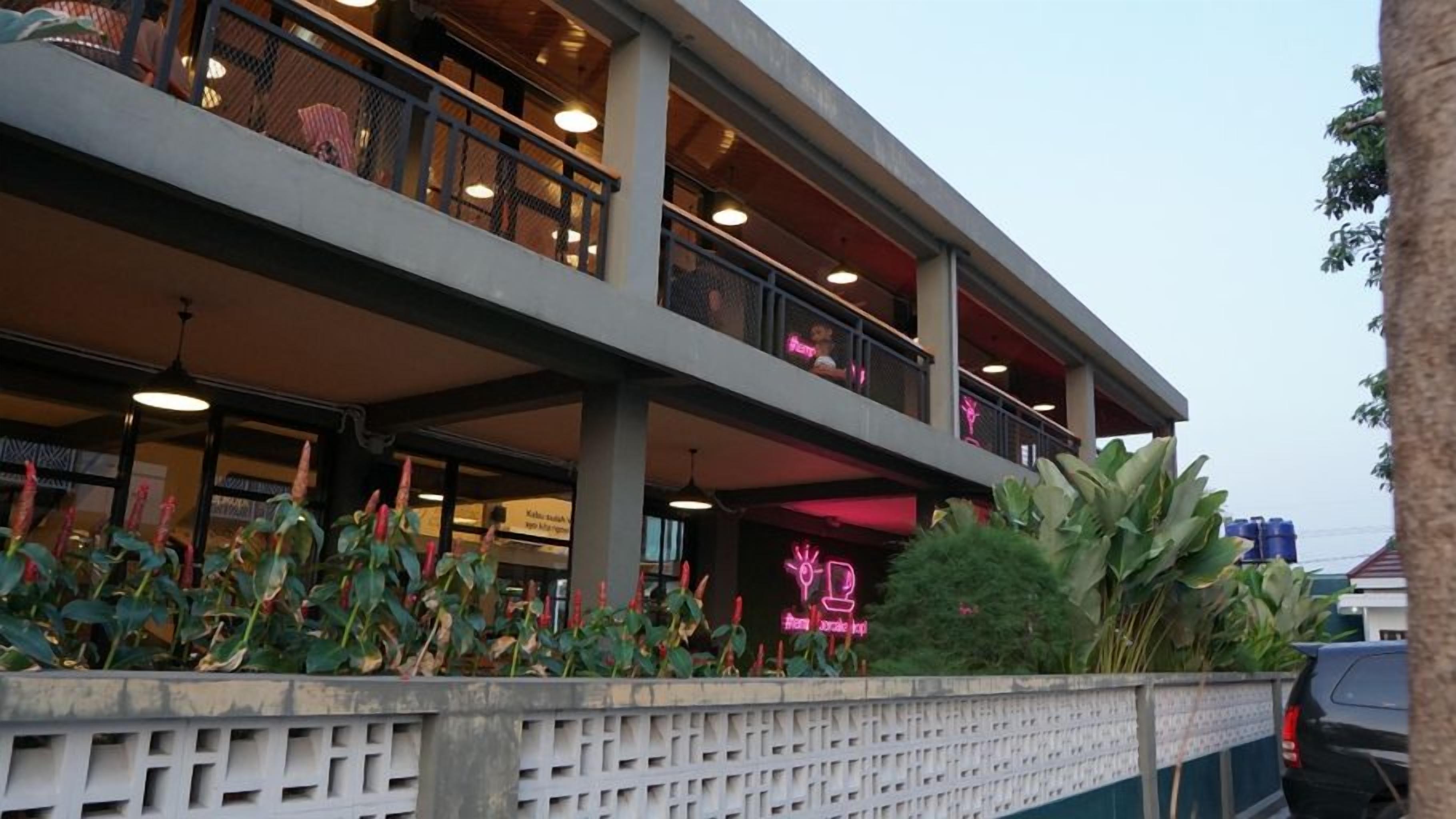 Un edifici de diverses plantes amb balcons, un cartell de neó i una paret de formigó amb plantes.