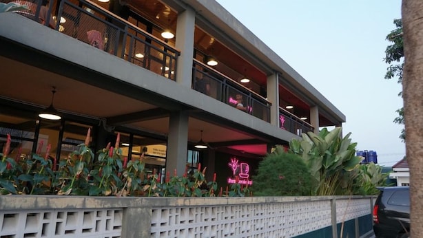 A multi-story building with balconies, a neon sign, and a concrete wall with plants. - Amaze Hotel Kediri (Ngasem)