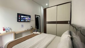 A hotel room with a bed, a television mounted on the wall, a wardrobe, and a small table with a kettle. - Amaze Hotel Kediri (Ngasem)