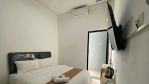 A hotel room with a bed, a bedside table with a cup and saucer, and a flat-screen TV mounted on the wall. - Amaze Hotel Kediri (Ngasem)