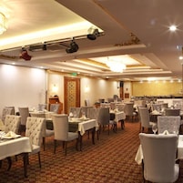 Comedor de hotel con varias mesas y sillas, candelabros y alfombra estampada.