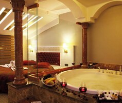 Una habitación de hotel con un espejo grande, una bañera, un frutero y una botella de vino.