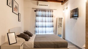Quarto com cama, mesas de cabeceira, televisão e janela com cortinas.