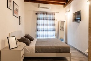 A bedroom with a bed, bedside tables, a TV, and a window with curtains. - La Naca by Wonderful Italy (Syracuse)