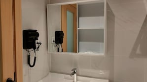 A bathroom with a white sink, a mirror, and a hairdryer mounted on the wall. - Samanea Boutique Apartment (Tangerang)