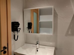 A bathroom with a white sink, a mirror, and a hairdryer mounted on the wall. - Samanea Boutique Apartment (Tangerang)