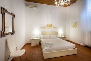 Quarto com cama, duas mesas de cabeceira, uma cadeira, um espelho e um candelabro.