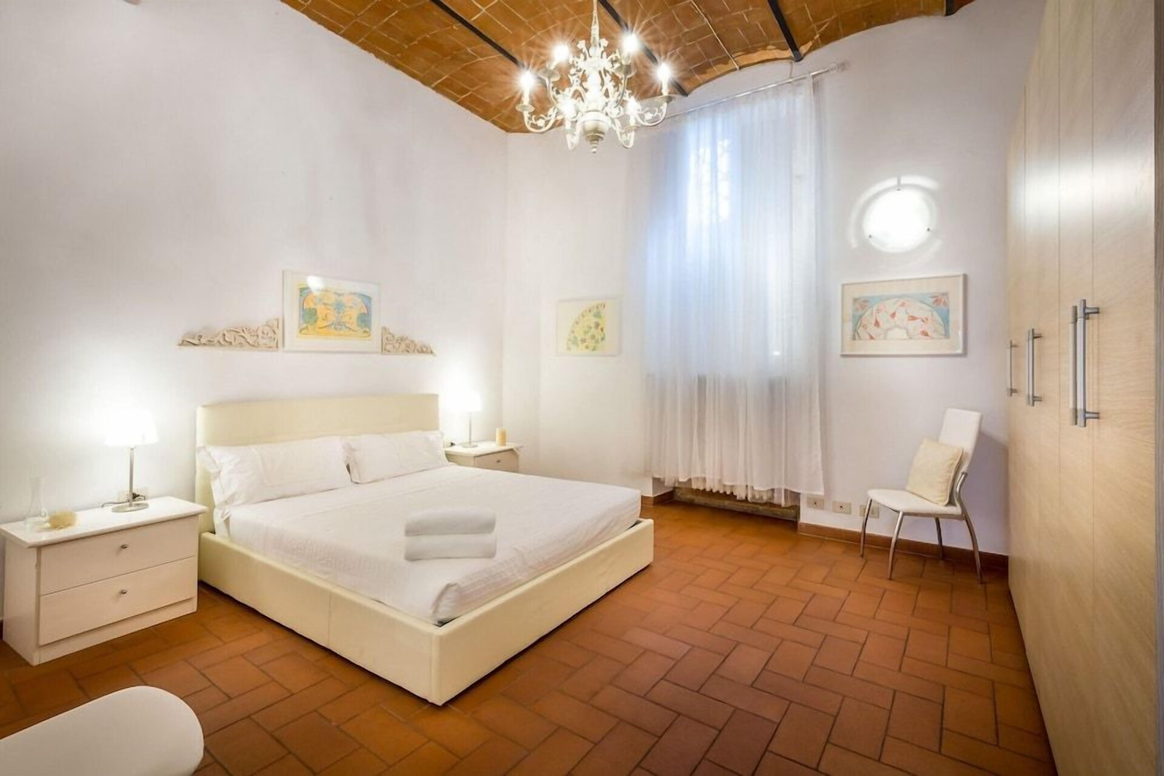 Une chambre à coucher avec un grand lit, des tables de chevet, une chaise et des œuvres d’art accrochées aux murs.