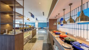 Eine moderne Hotelhalle mit einer langen Rezeption, einer Kaffeebar und einem Buffet mit verschiedenen Speisen.