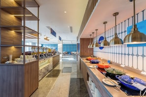 En moderne hotellobby med en lang receptionsdisk, en kaffebar og et buffetområde med forskellige retter.