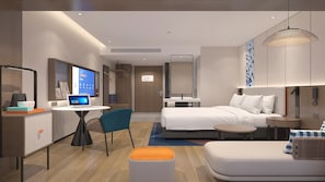 Et moderne hotelværelse med seng, skrivebord, stol, lille bord, sofa og hængende lampe.