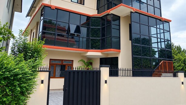 Una casa moderna de dos pisos con ventanas grandes y un portón negro.